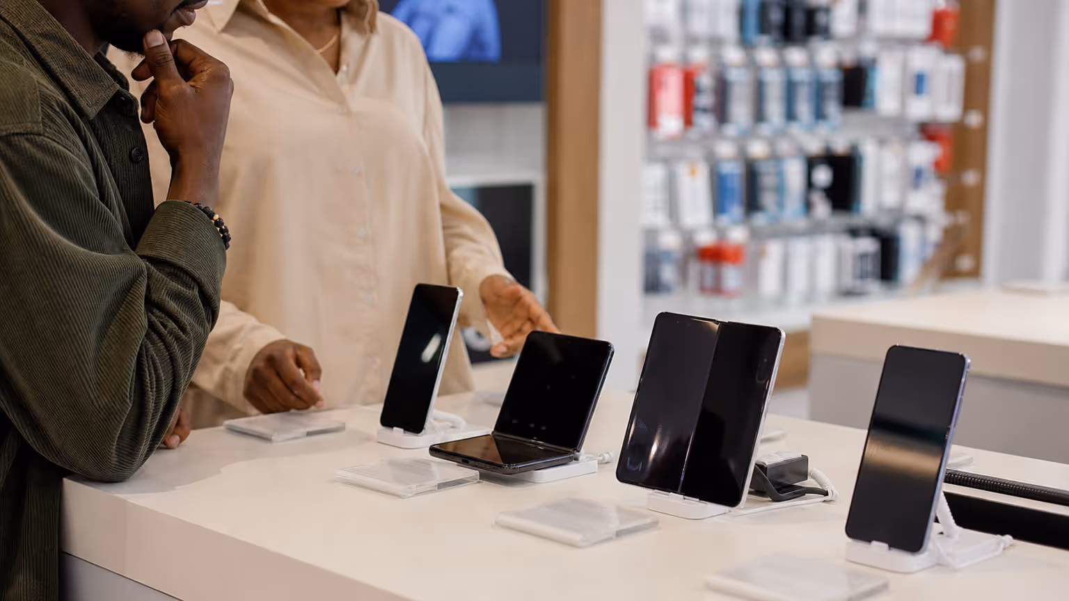 Realistic foldable-phone launch decision scene in an electronics retail setting with no logos or readable text