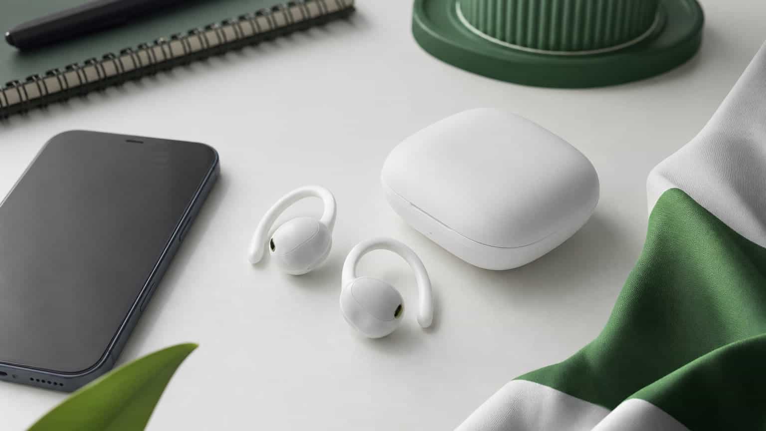 Open-fit white wireless earbuds and charging case on a clean desk beside a smartphone