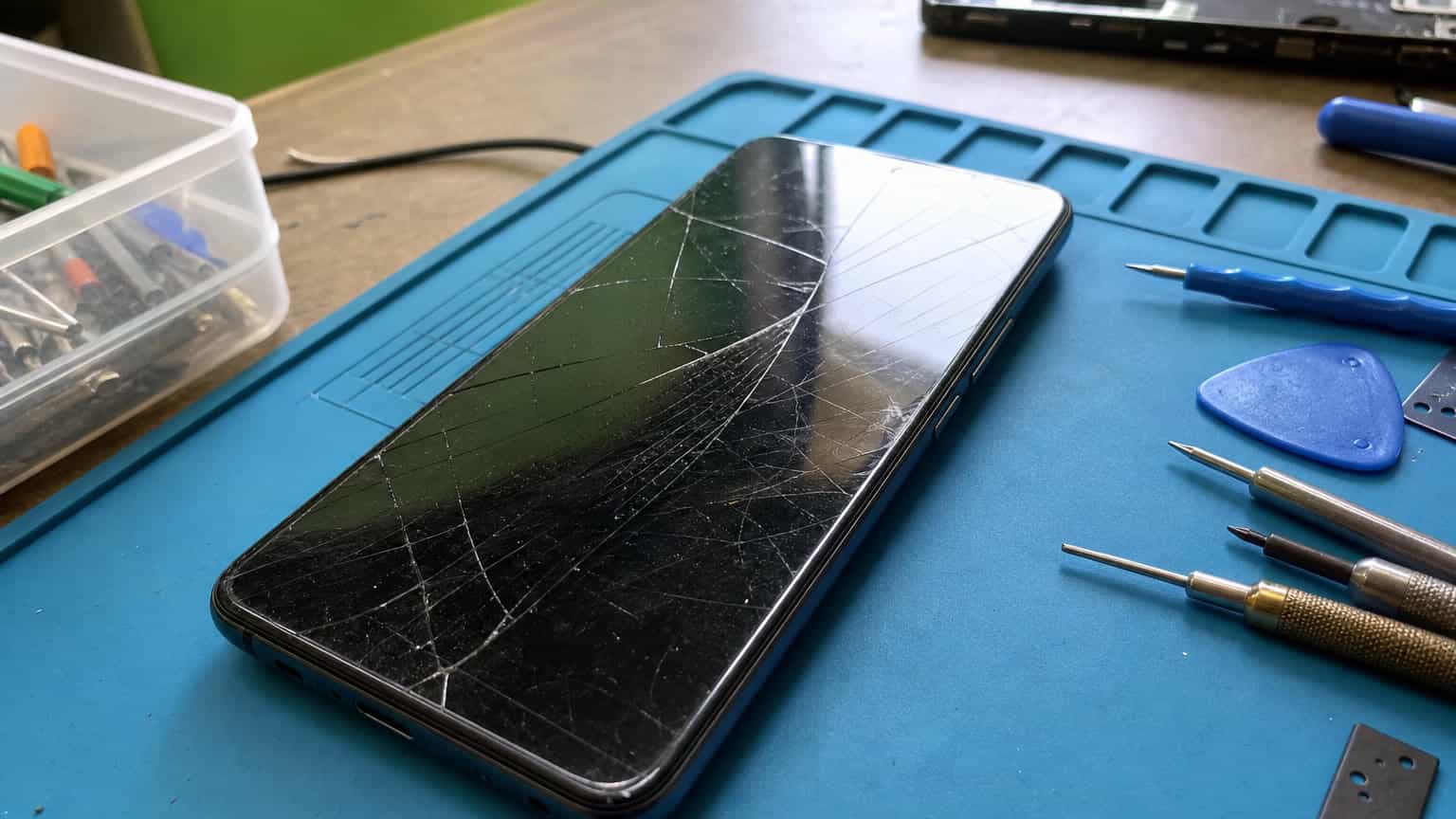 Cracked smartphone screen on a repair bench with tools nearby