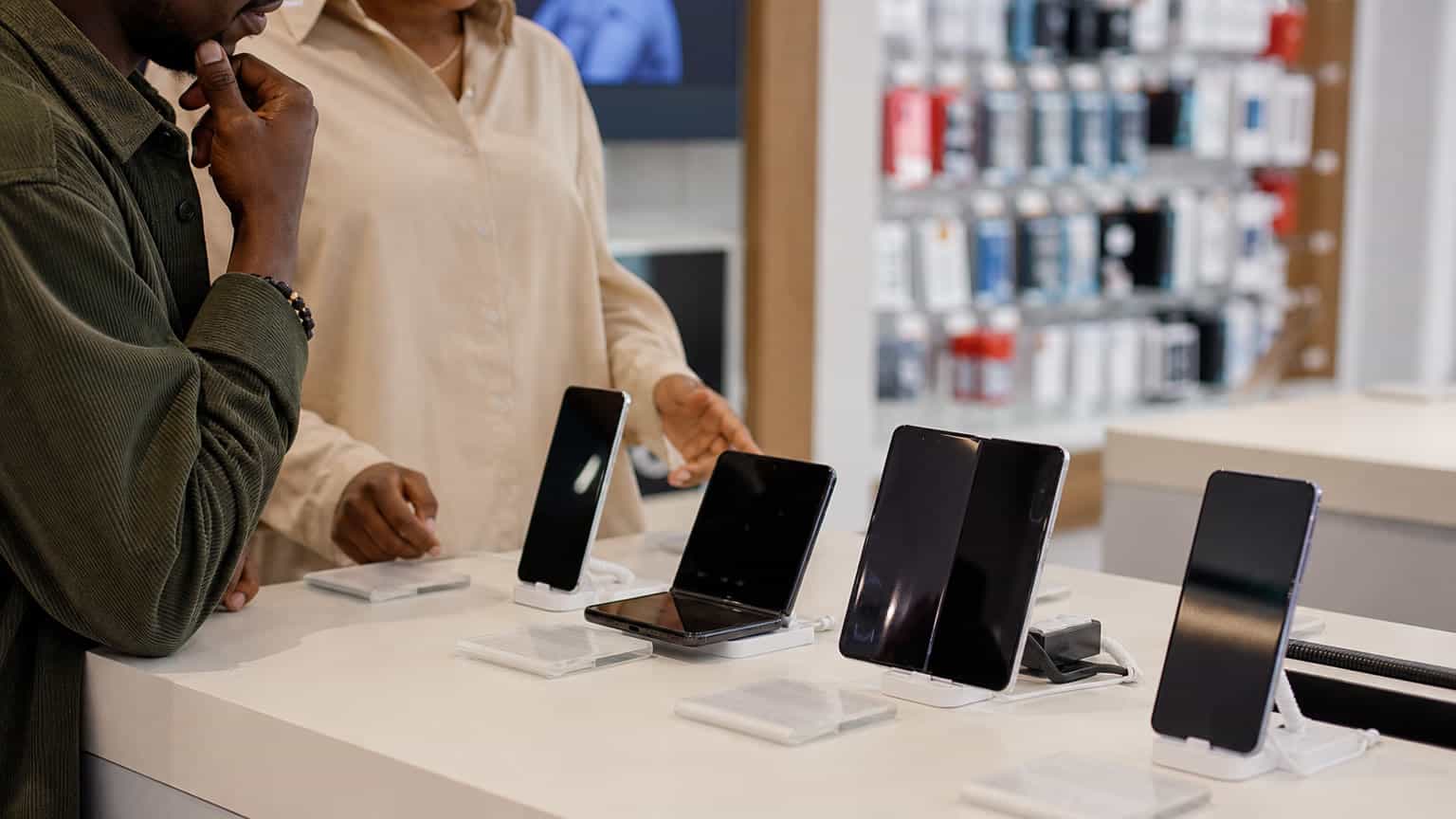 Realistic foldable-phone launch decision scene in an electronics retail setting with no logos or readable text