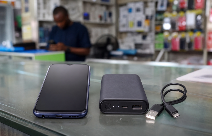 Entry-level smartphone beside a power bank and charging cable in a phone shop