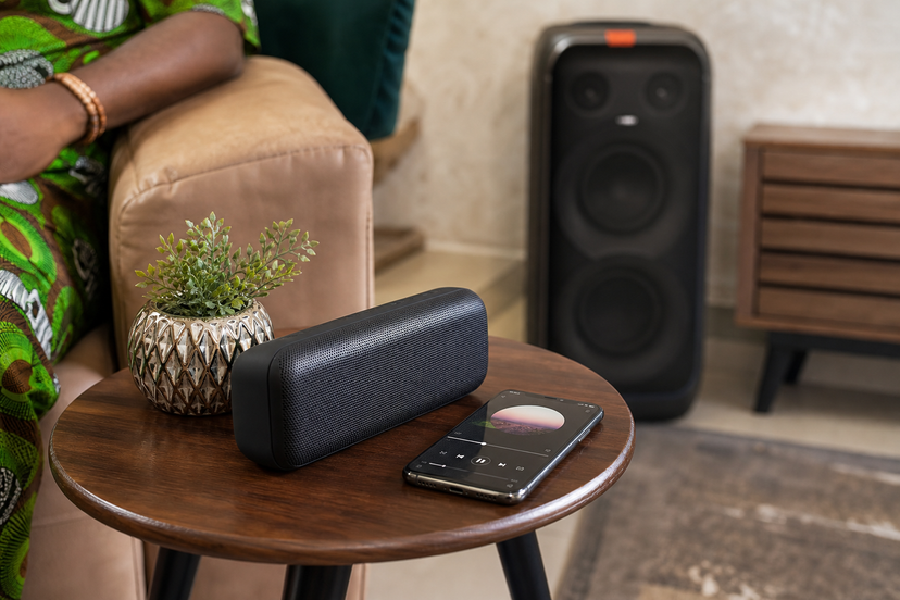 Portable speaker on a living-room table with a phone and a larger speaker in the background