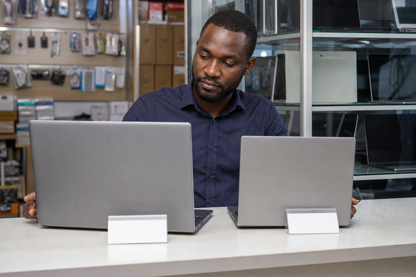 Buyer comparing two used business laptops on a gadget store counter